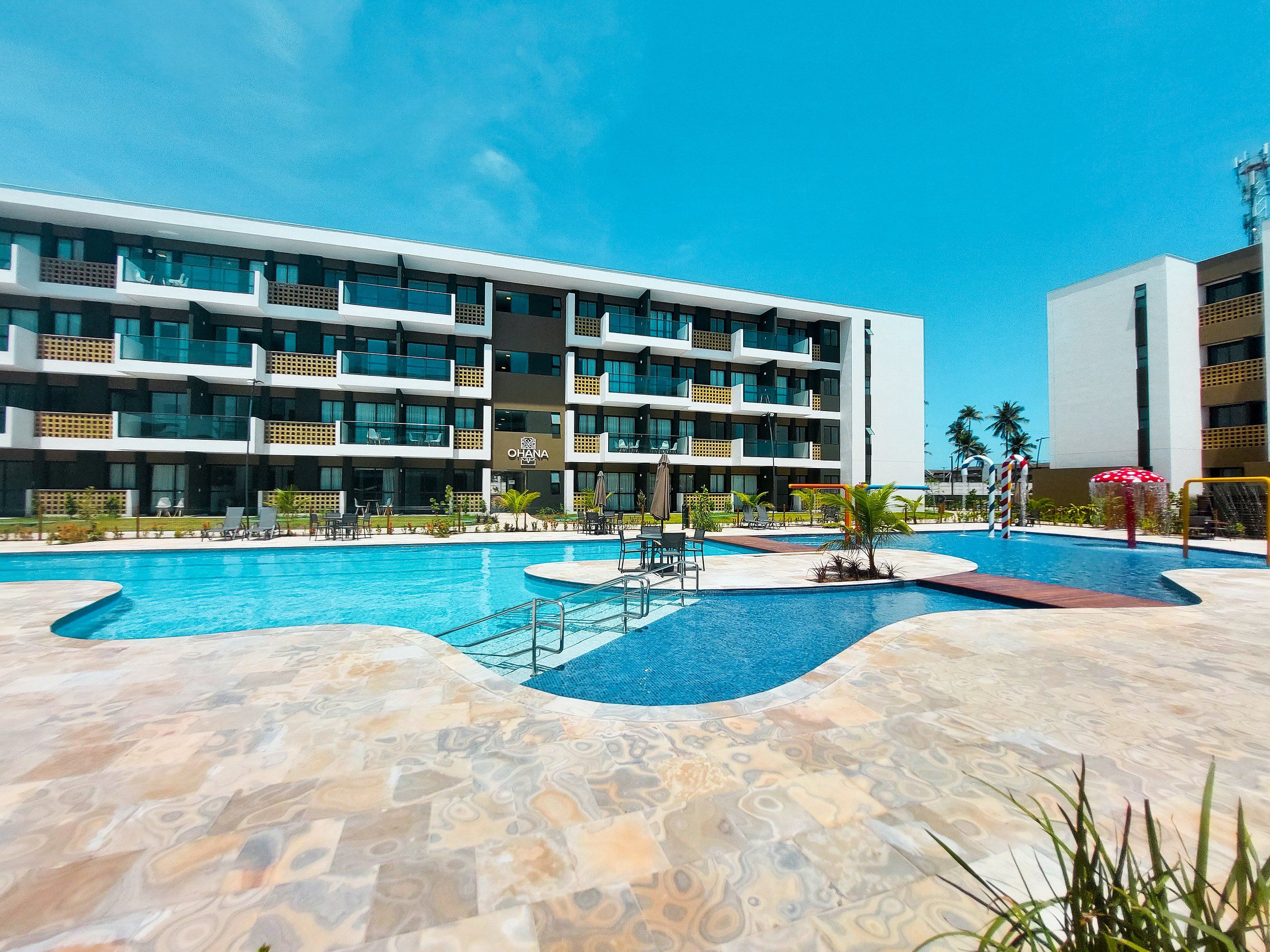 A hotel with a swimming pool, multiple balconies, and a clear blue sky.