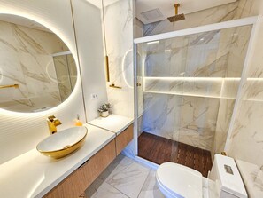A modern bathroom with a large oval mirror, a gold bowl sink, a glass-enclosed shower, and a wooden vanity. - Mana Beach Experience- Porto de Galinhas (Ipojuca)