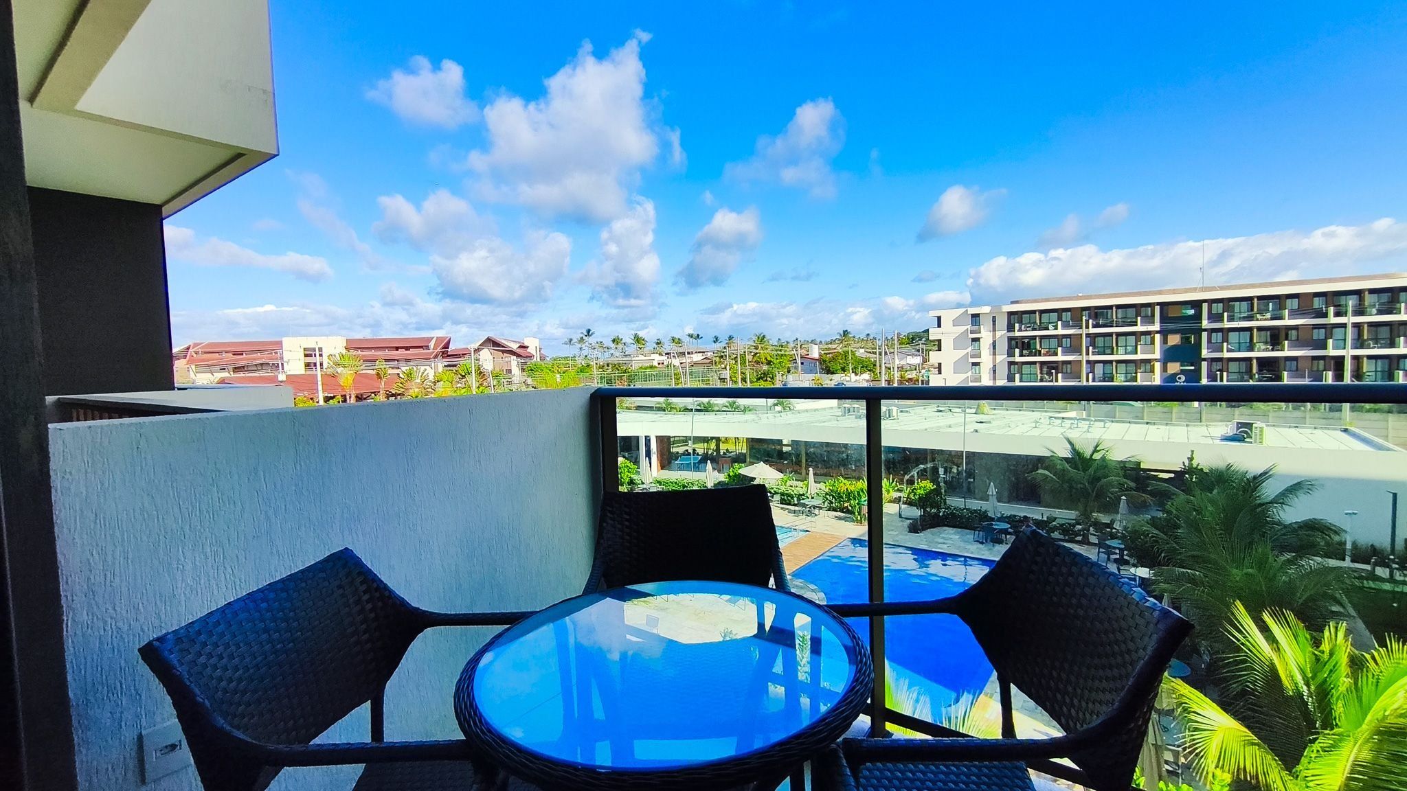 Un balcón con dos sillas y una mesa, con vistas a una piscina y edificios.