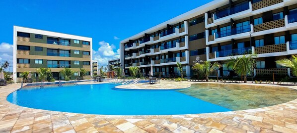 A hotel with a large swimming pool, multiple balconies, and a clear blue sky.