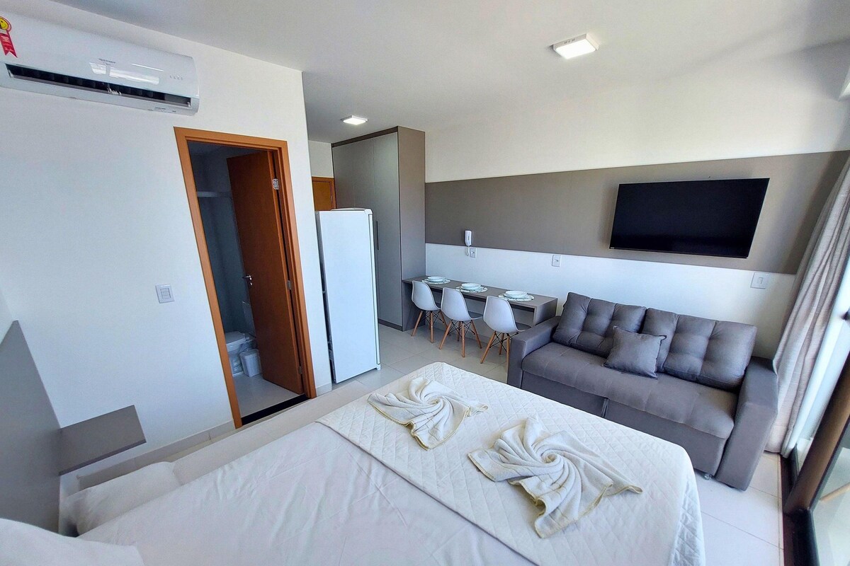 A hotel room with a bed, a sofa, a dining area, and a TV.