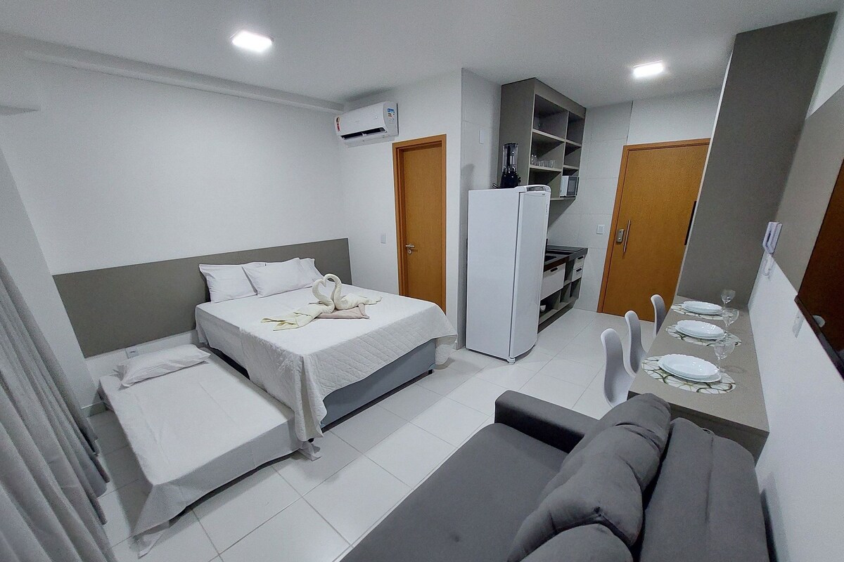 A compact hotel room with a bed, a sofa, a kitchenette, and a built-in wardrobe.