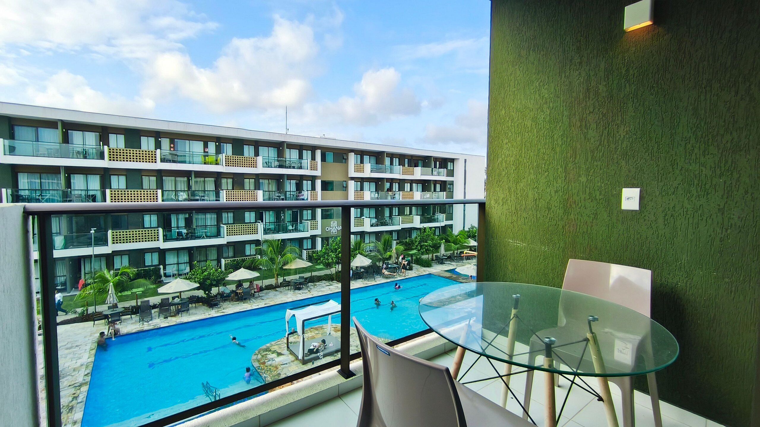 A modern hotel with a glass balcony overlooking a pool area.