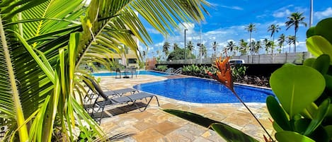 Uma área de piscina com espreguiçadeiras, palmeiras e céu azul límpido.