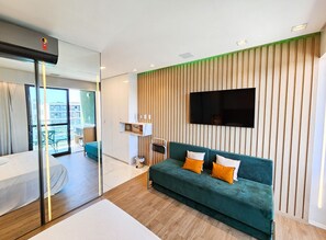 A modern hotel room with a green sofa, wooden panel wall, and a flat-screen TV. - Mana Beach Experience- Porto de Galinhas (Ipojuca)
