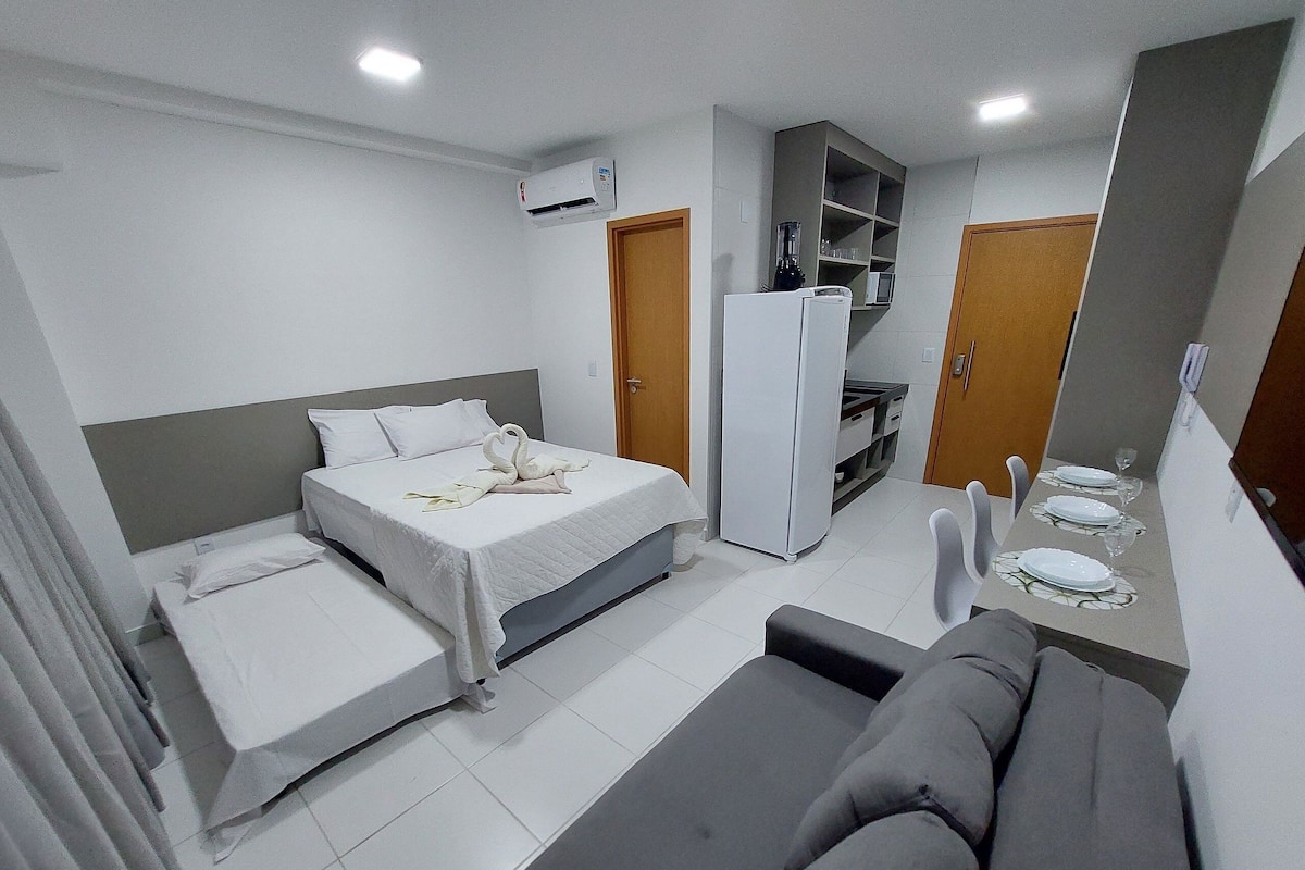 Quarto de hotel pequeno com cama, sofá, cozinha compacta e armário embutido.