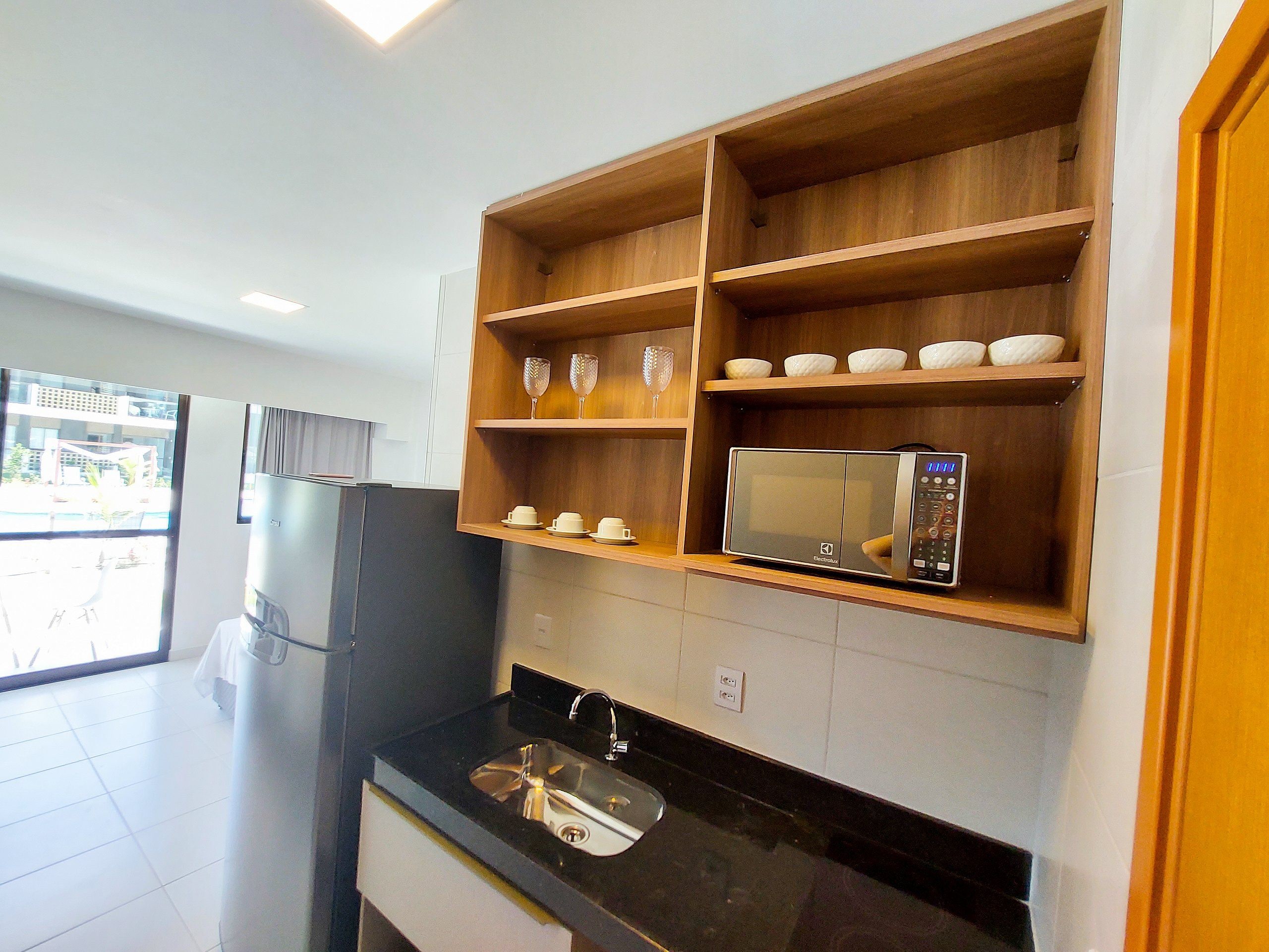 A modern kitchen with a built-in microwave, wooden shelves, and a black countertop.