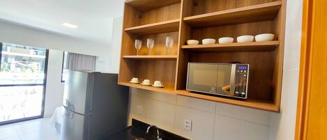 A modern kitchen with a built-in microwave, wooden shelves, and a black countertop.
