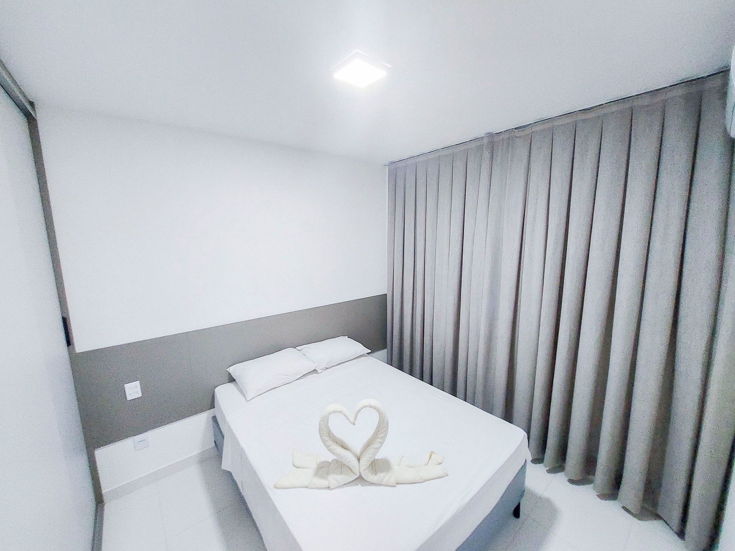 A hotel room with a bed, curtains, and a heart-shaped towel decoration.