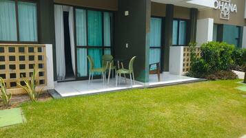 Exterior moderno de un hotel con un área de estar al aire libre cubierta, un césped cuidado y un cartel con el nombre del hotel.