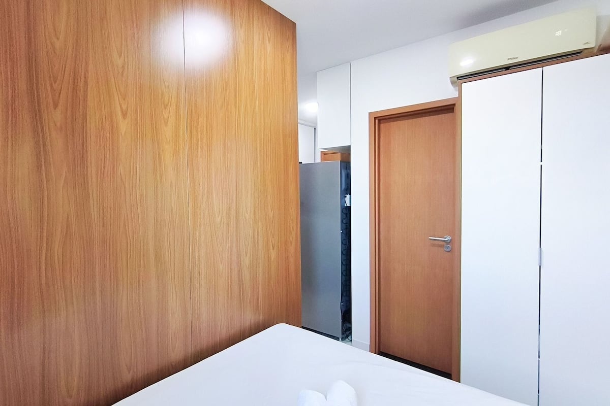 Um quarto com guarda-roupa de madeira, cama branca e porta fechada.