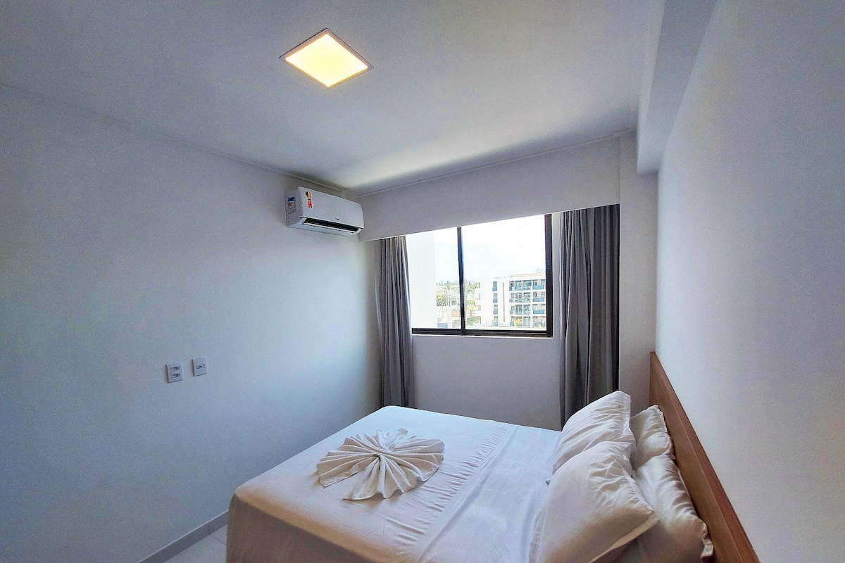 Quarto de hotel com cama, ar condicionado, janela com cortinas e vista para prédios.