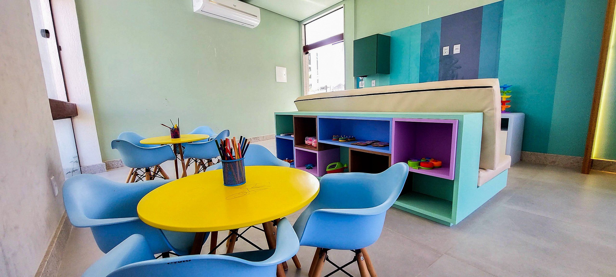 A classroom with blue chairs, a yellow table, and colorful storage units.