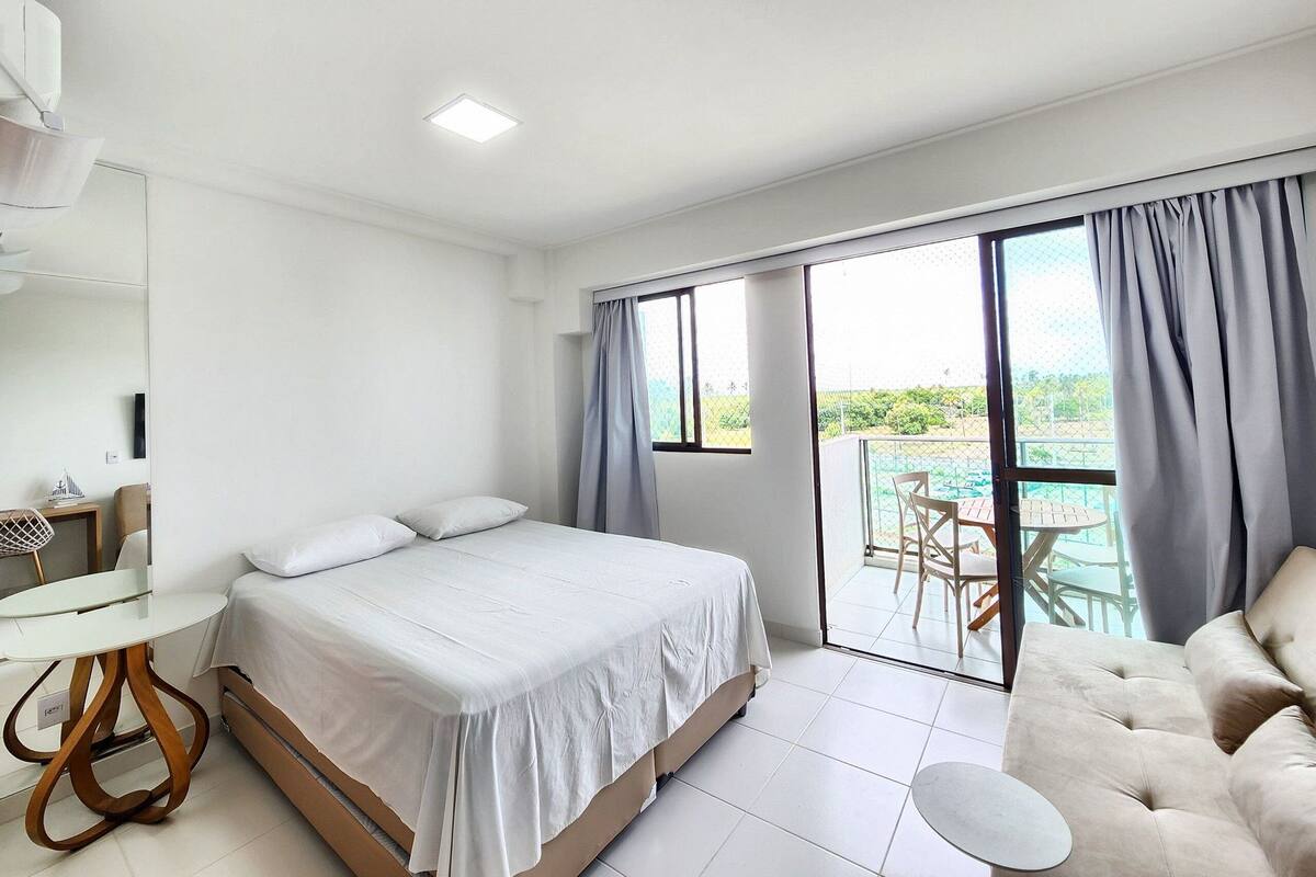 Quarto com cama, uma mesinha, um sofá e varanda com vista.