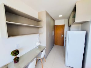 A narrow kitchen with a refrigerator, a glass table, and a potted plant.