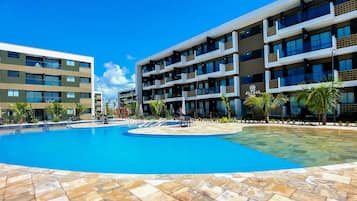 Un hotel con una amplia piscina, varios balcones y un cielo azul despejado.