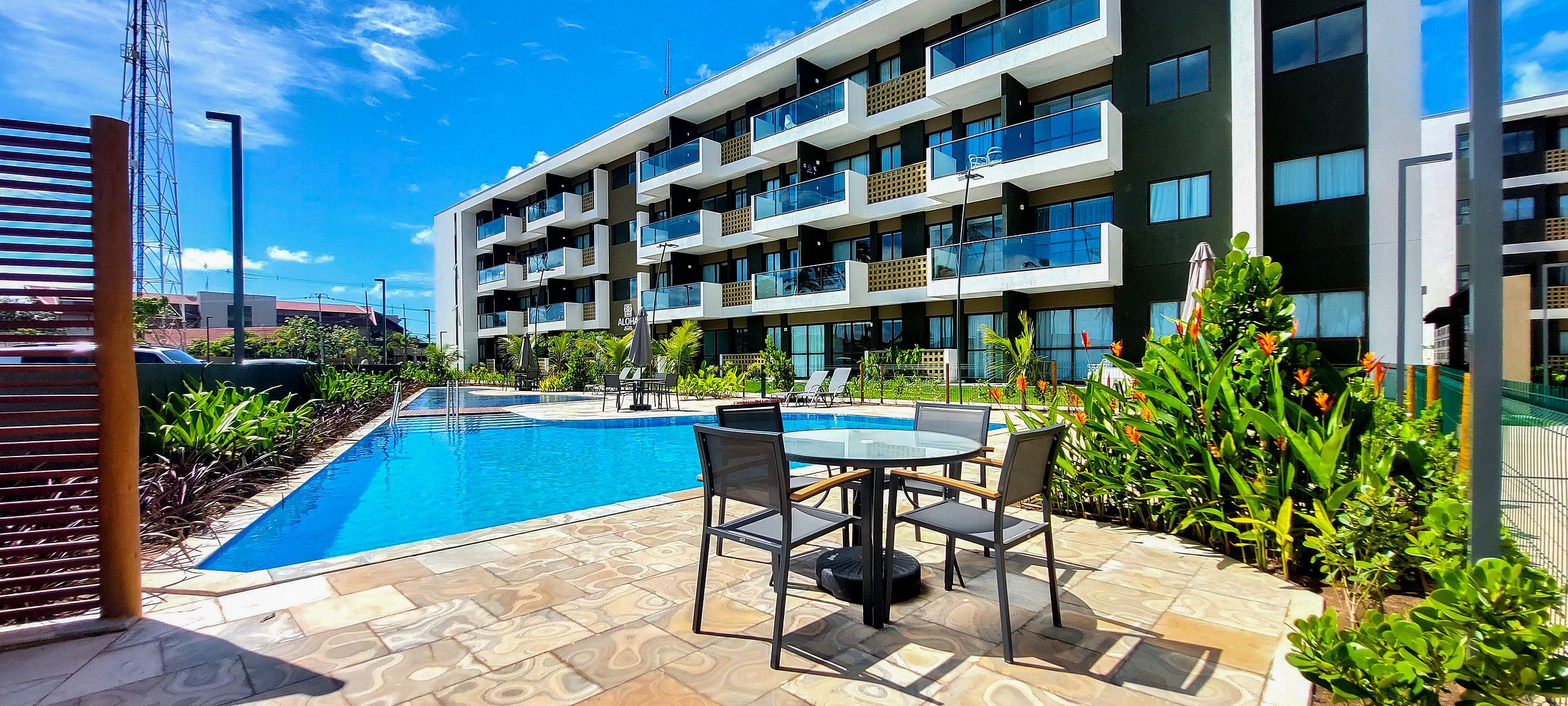 A modern hotel with a swimming pool, outdoor seating, and lush greenery.