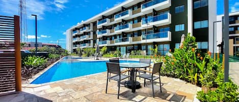 A modern hotel with a swimming pool, outdoor seating, and lush greenery.
