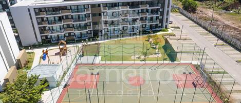 A multi-story building with balconies, a basketball court, and a playground.
