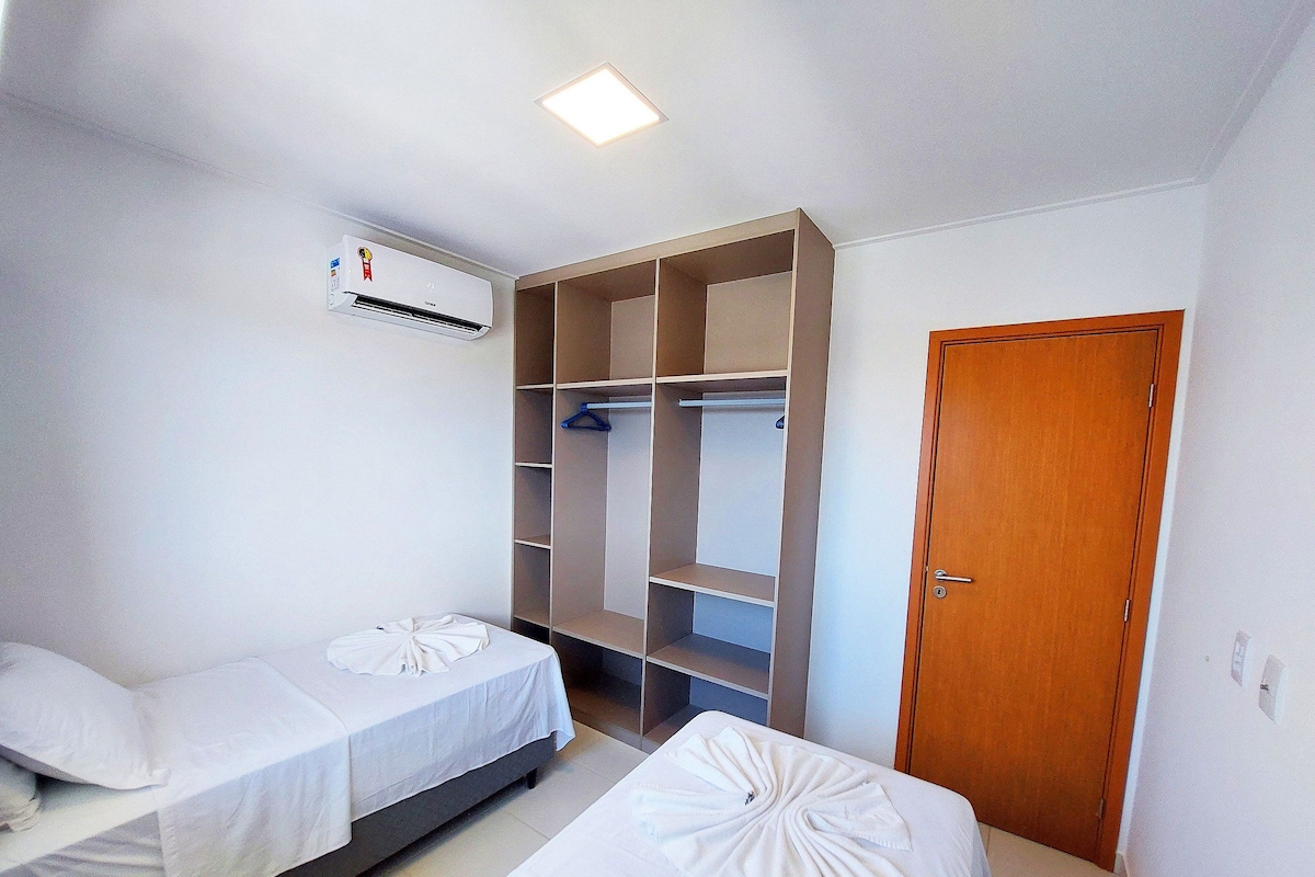 A hotel room with two beds, a wardrobe, and an air conditioning unit.