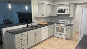 Uma cozinha moderna com armários brancos, bancada preta, micro-ondas, forno e pia.