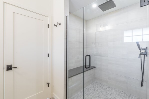 Une salle de bain moderne avec une douche à l’italienne en verre, une porte blanche et un sol carrelé.