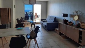 A modern living room with a dining area, a sofa, a coffee table, and a TV on a wooden cabinet. - Comfortable T3 with terrace 5 minutes walk from Saint-Leu beach (Saint-Leu)