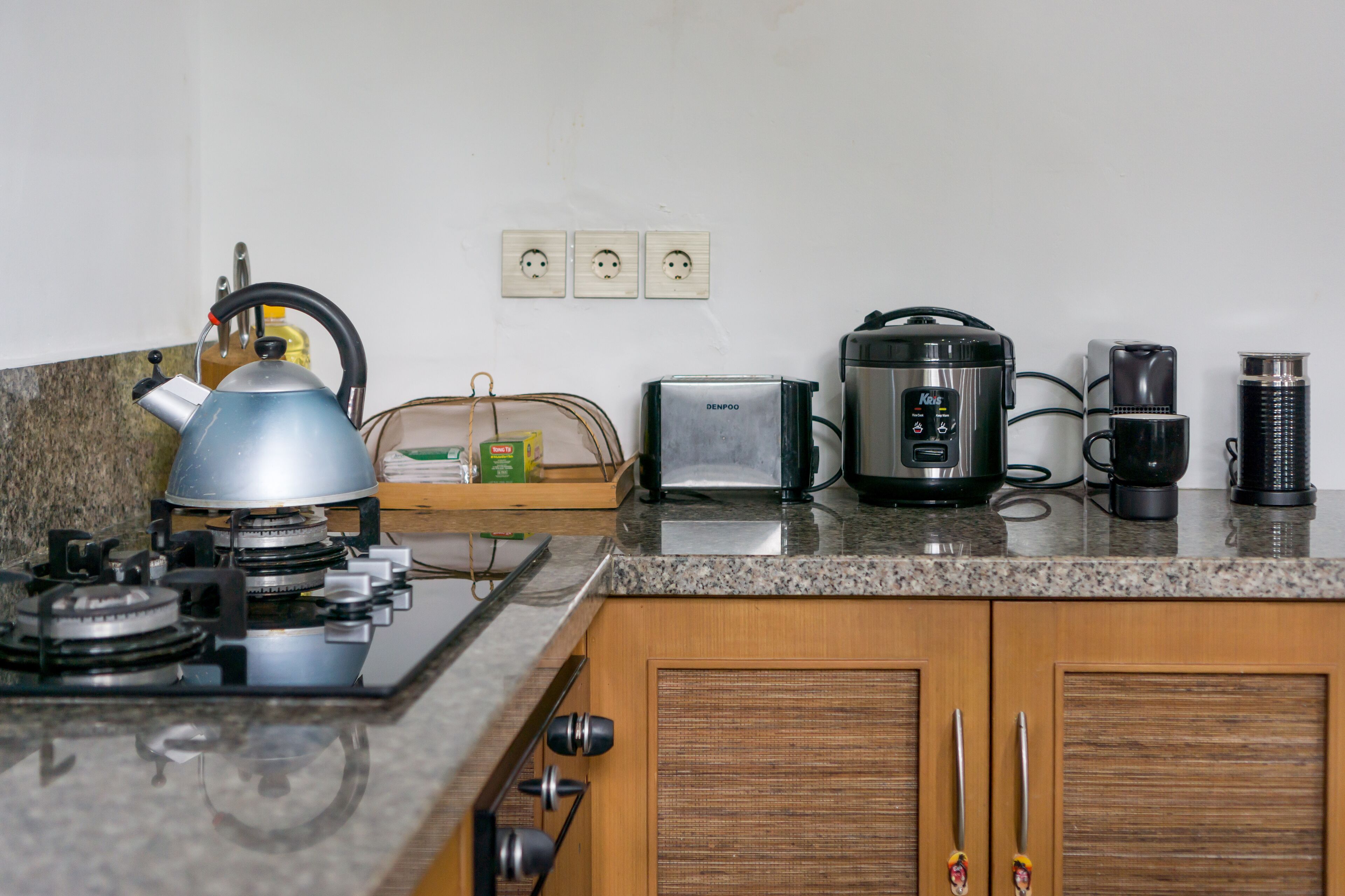 Una cocina con estufa a gas, hervidor, tostadora, cafetera y licuadora.
