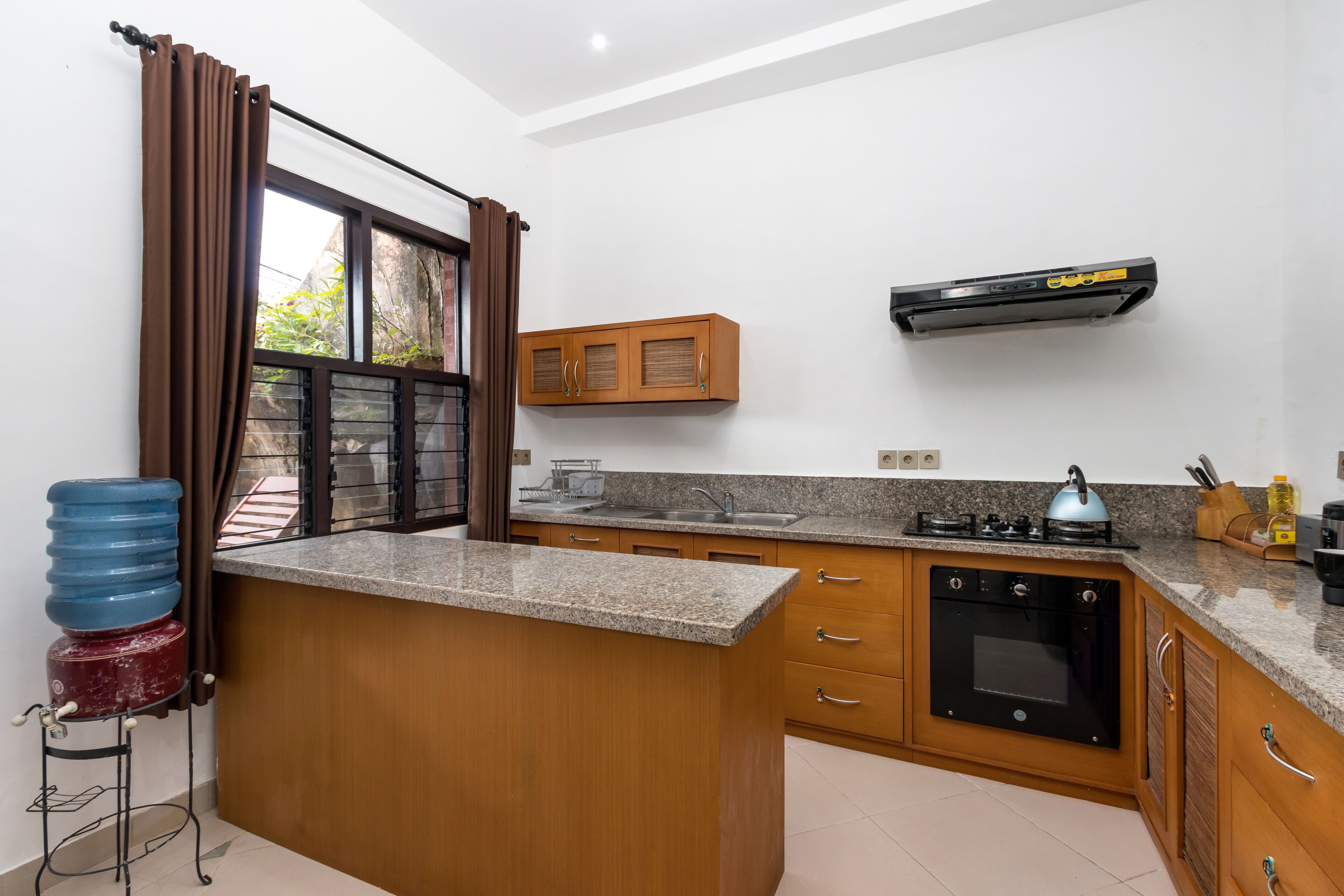 A kitchen with granite countertops, wooden cabinets, a built-in oven, and a window with curtains.