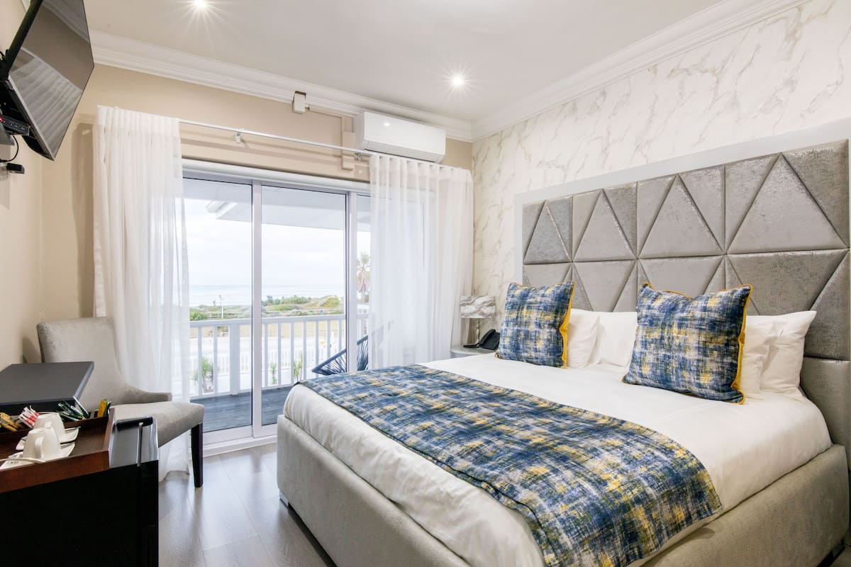 Een slaapkamer met een groot bed, een bureau en een stoel. Er is een balkon met uitzicht op zee.