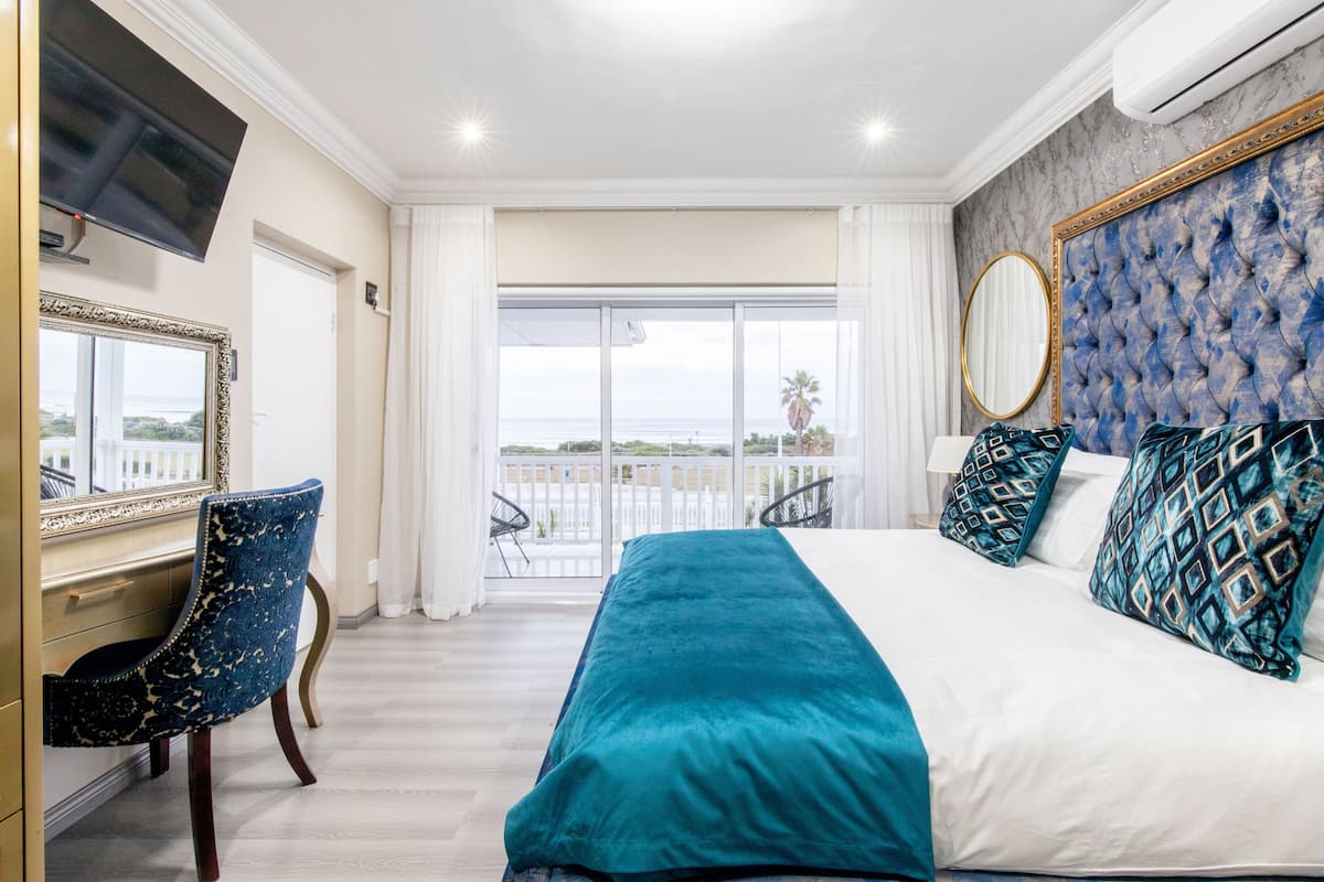 Een slaapkamer met een groot bed, een bureau en uitzicht op zee door een schuifdeur.