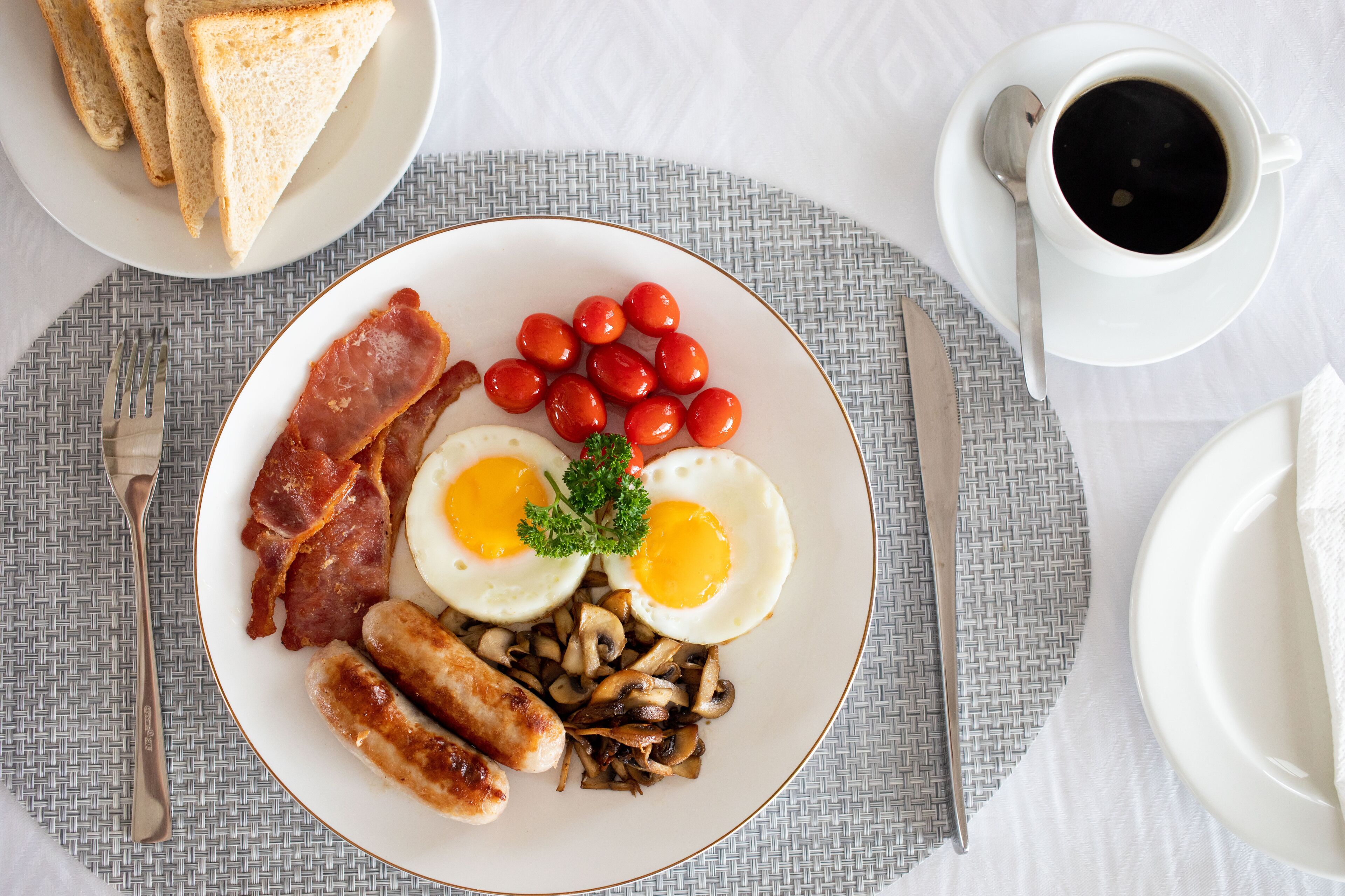 A breakfast plate with eggs, bacon, sausages, mushrooms, cherry tomatoes, and toast.
