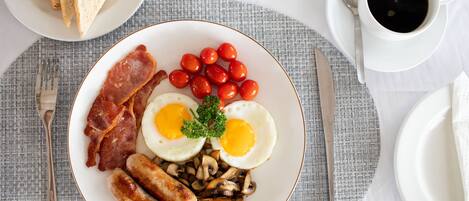 A breakfast plate with eggs, bacon, sausages, mushrooms, cherry tomatoes, and toast.