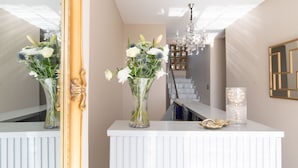 Ein Empfangsbereich mit einer weißen Theke, zwei Blumenvasen, einer Chandelierleuchtre und einer Treppe im Hintergrund.