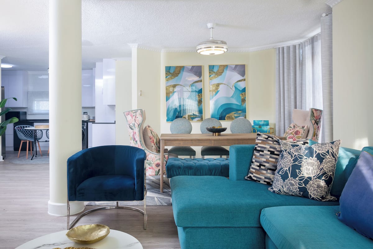 Een moderne woonkamer met een blauwgroene bank, een blauwe fauteuil en een eethoek met een houten tafel en stoelen.