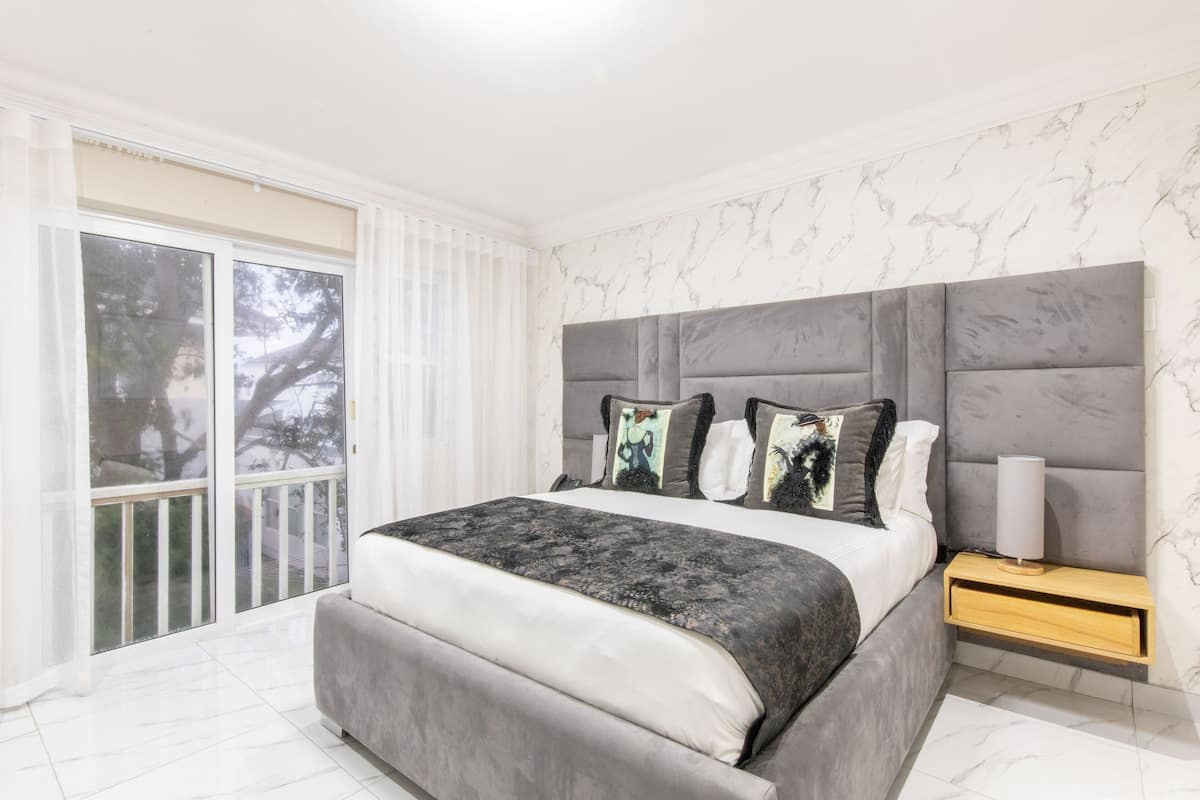Een moderne slaapkamer met een groot bed, een nachtkastje en uitzicht op bomen.