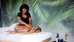 Ein Massagezimmer mit Liege, Handtuch, Tablett mit Flaschen und Wand mit Palmenblattmuster.