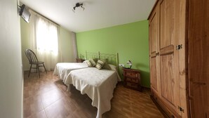 Ein Schlafzimmer mit zwei Betten, einem Holzschrank, einem Nachttisch, einem Sessel und einer Lampe.