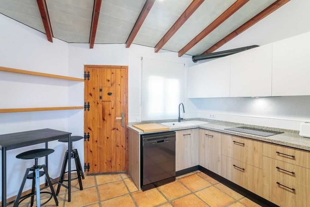 Une cuisine compacte dotée de meubles en bois, d’un lave-vaisselle, d’un évier et d’un petit coin bar avec des tabourets.