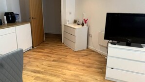 A small, tidy room with a wooden floor, a white desk with drawers, a television, and a door leading to another room. - Large Private Flat in City Centre Leeds (Leeds)