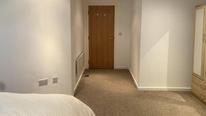 A narrow hallway with a wooden door at the end, carpeted floor, and a bed on the left. - Large Private Flat in City Centre Leeds (Leeds)