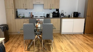 A compact kitchen with wooden cabinets, a dining table with four chairs, and a coffee machine. - Large Private Flat in City Centre Leeds (Leeds)