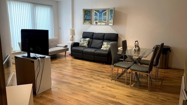 A modern living room with a black sofa, a glass dining table, and a TV on a stand. - Large Private Flat in City Centre Leeds (Leeds)