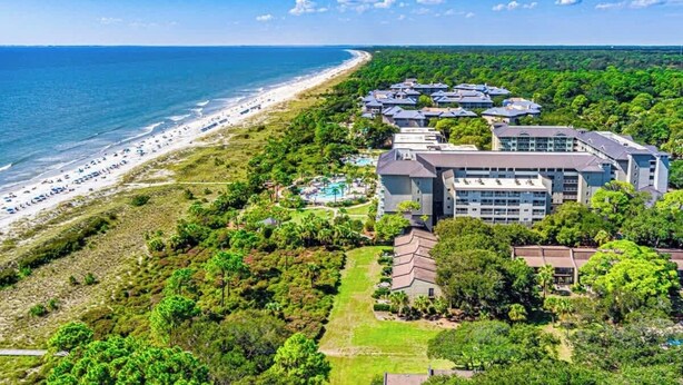 An aerial view of a coastal hotel with multiple buildings, a beach, and lush greenery.