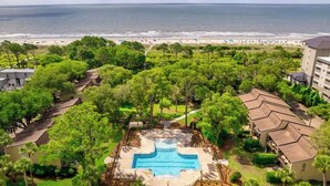 A resort with a central swimming pool, surrounded by lush greenery and a beach view.
