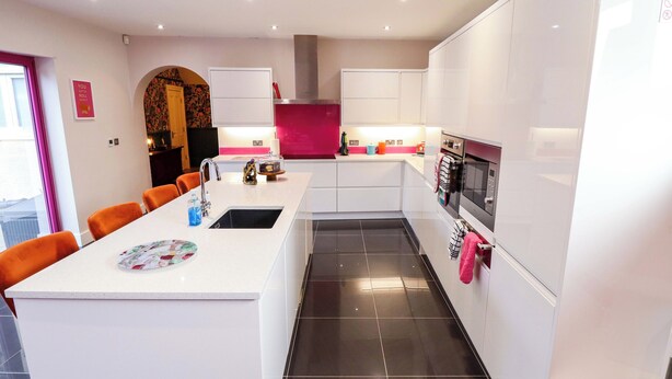 Une cuisine moderne avec des meubles blancs, un îlot central, un four en acier inoxydable et un coin repas avec des chaises orange.