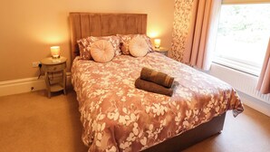 Une chambre avec un grand lit, deux tables de chevet avec des lampes, une fenêtre avec des rideaux et un radiateur.