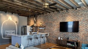 Un espace de vie moderne avec des murs en briques apparentes, un coin cuisine, un bar avec des tabourets, un téléviseur à écran plat et un coin salon confortable avec un canapé et une table basse.