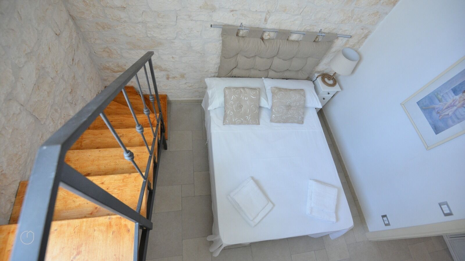 A bedroom with a bed, a wooden staircase, and a stone wall.