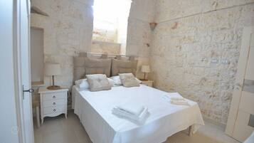 A bedroom with a stone wall, a bed with white linens, two bedside tables with lamps, and a door.